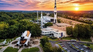 A space shuttle on display, a launch tower, and a building with a parking lot. - Beautiful New Home - Min to Airport and Space Museum! (Madison)