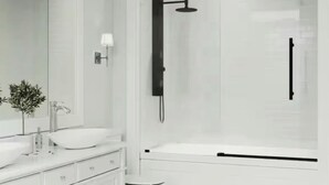 A modern bathroom with a white vanity, a large mirror, a toilet, and a glass-enclosed shower area. - Beautiful New Home - Min to Airport and Space Museum! (Madison)