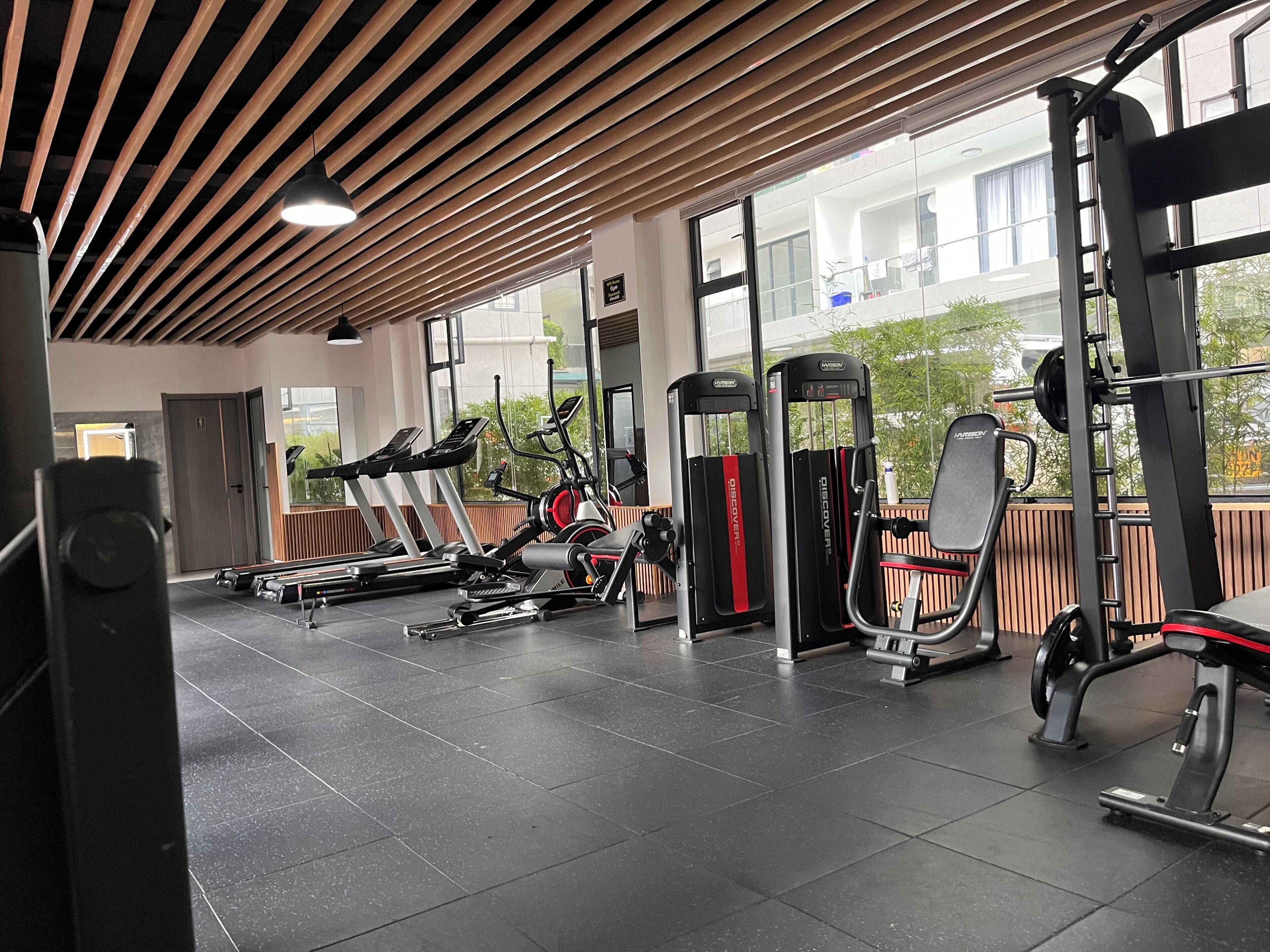 A gym with exercise equipment, large windows, and a wooden ceiling.