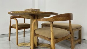 Una mesa redonda de madera con una cesta trenzada encima, flanqueada por dos sillas de madera con asientos acolchados.