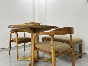 Ein runder Holztisch mit einem geflochtenen Korb darauf, begleitet von zwei Holzstühlen mit gepolsterten Sitzflächen.