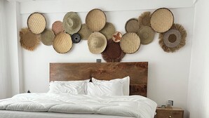 Un dormitorio con estructura de cama de madera, ropa de cama blanca, alfombra con estampado de cebra y una pared decorada con sombreros tejidos.