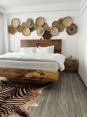 Ein Schlafzimmer mit einem Bettgestell aus Holz, weißer Bettwäsche, einem Teppich mit ZEBRA-MUSTER und einer Wand, die mit gewebten Hüten dekoriert ist.