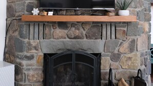 A stone fireplace with a flat-screen TV mounted above it, a small plant on the mantel, and a log storage area below.
