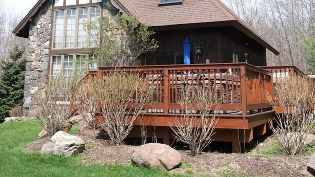 A large, two-story house with a stone facade, a wooden deck, and a clear sky.