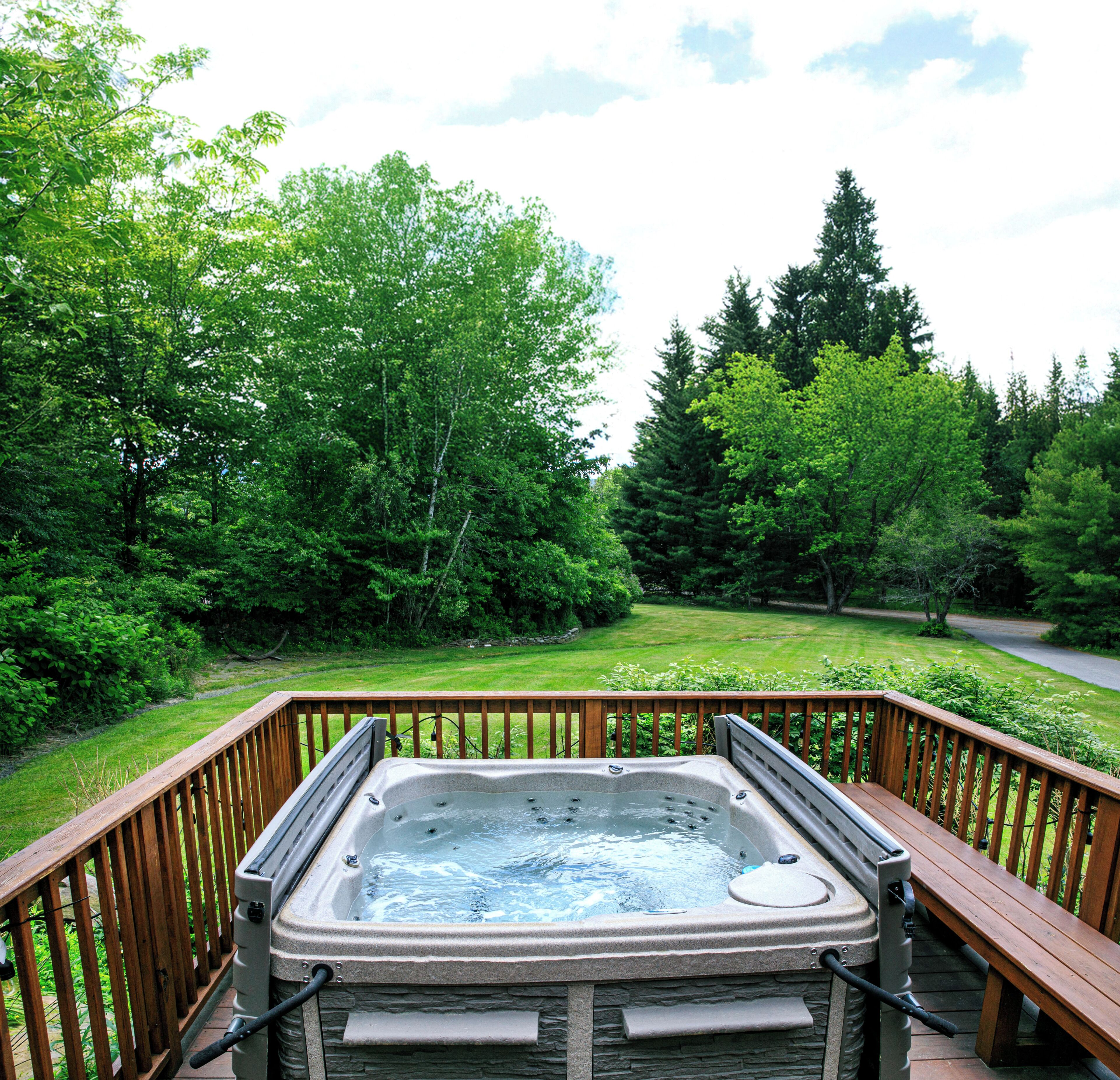 Un bain à remous sur une terrasse en bois, avec vue sur un paysage verdoyant et luxuriant ainsi que sur des arbres.