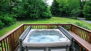 A hot tub on a wooden deck with a view of a lush green landscape and trees.