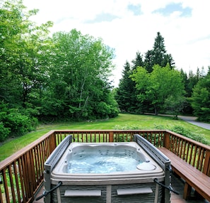 A hot tub on a wooden deck with a view of a lush green landscape and trees.