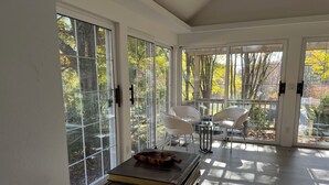 Una habitación moderna con amplios ventanales de vidrio, una mesa de madera y dos sillas blancas.