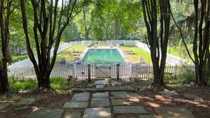 Un sendero de piedra que conduce a una piscina con una valla blanca y árboles.
