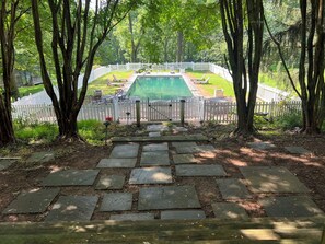 A stone pathway leading to a pool with a white fence and trees.