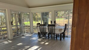 Un comedor iluminado por el sol con una mesa y sillas, puertas de cristal grandes y vistas a un jardín.