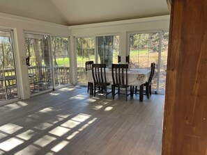 A sunlit dining area with a table and chairs, large glass doors, and a view of a garden.