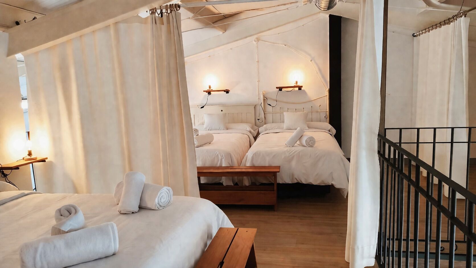 A room with two beds, a wooden bench, and a wall-mounted light fixture.