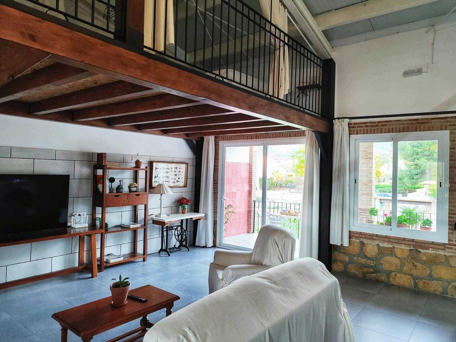 A spacious living area with a high ceiling, a TV, a wooden bench, a table, and a sofa.