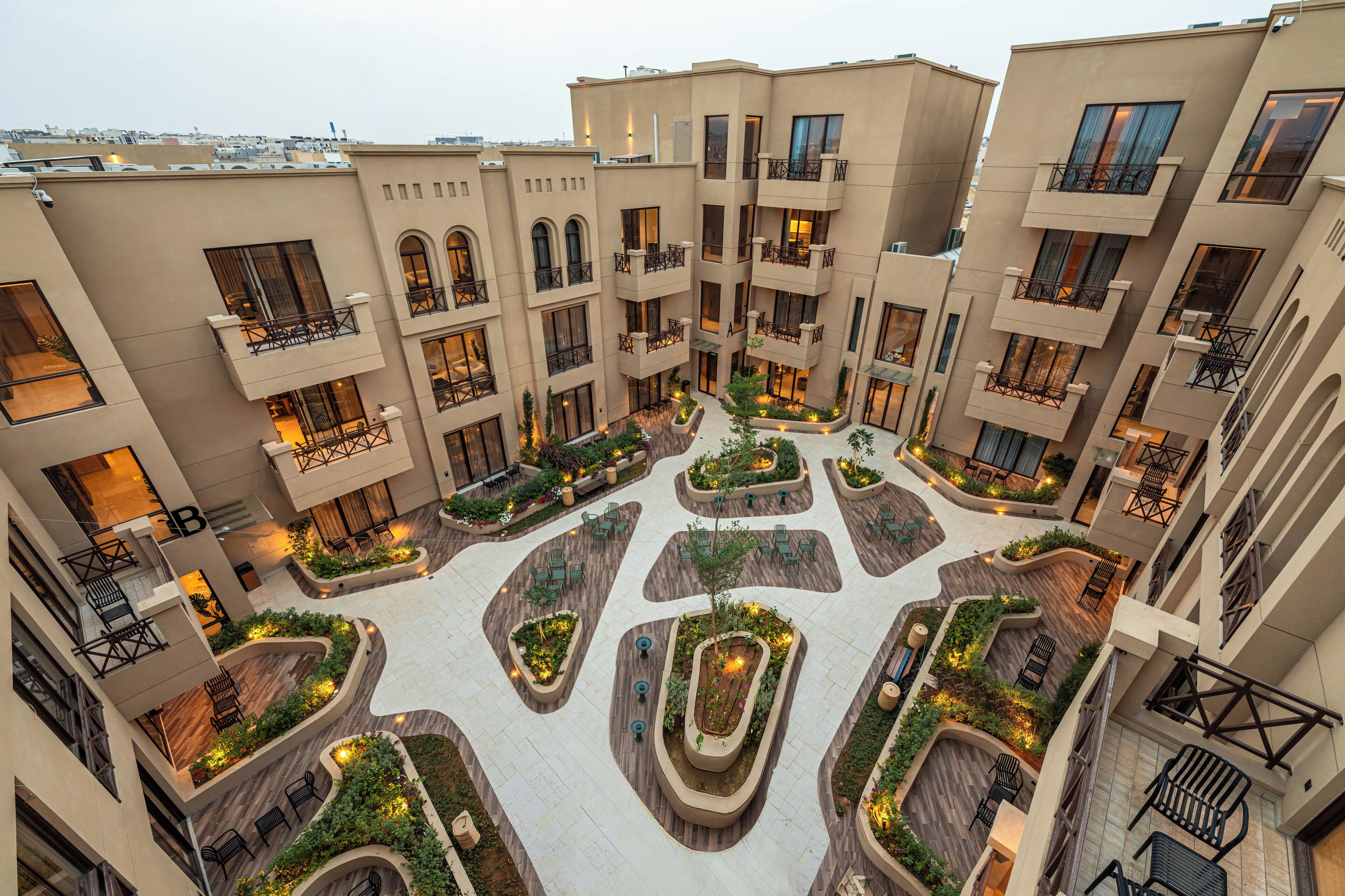 Et hotel med flere etager, der har en central gårdsplads med plantekasser og siddepladser.