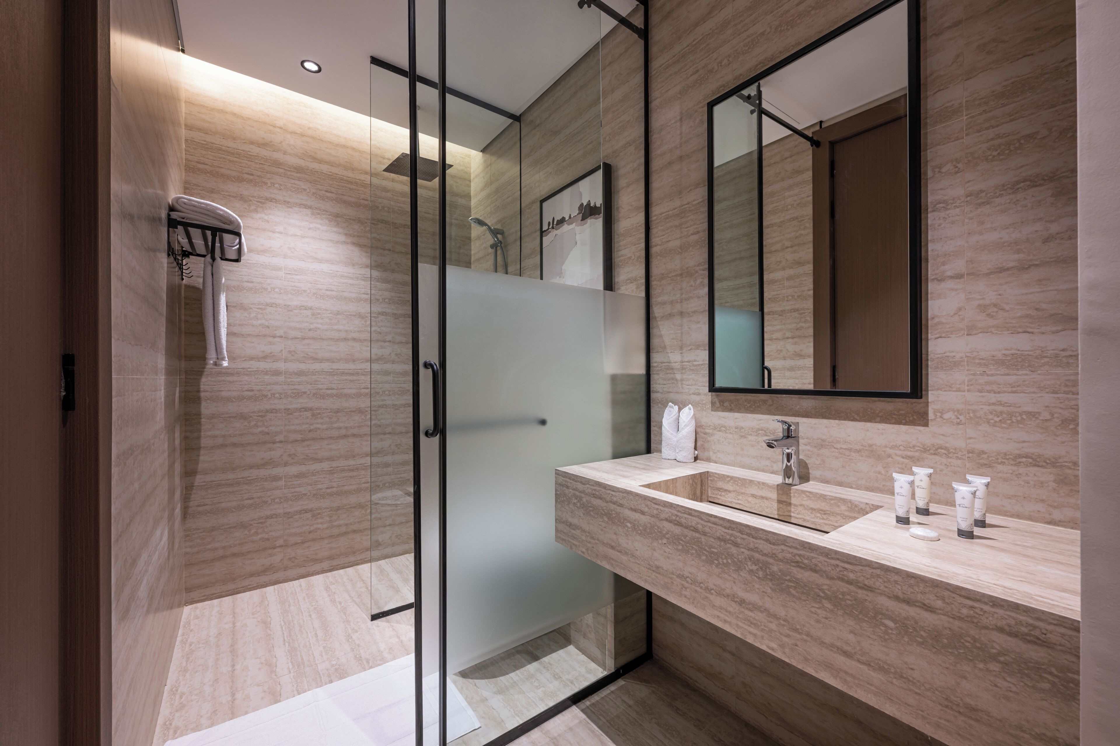 A modern bathroom with a glass shower enclosure, a large mirror, and a marble countertop.