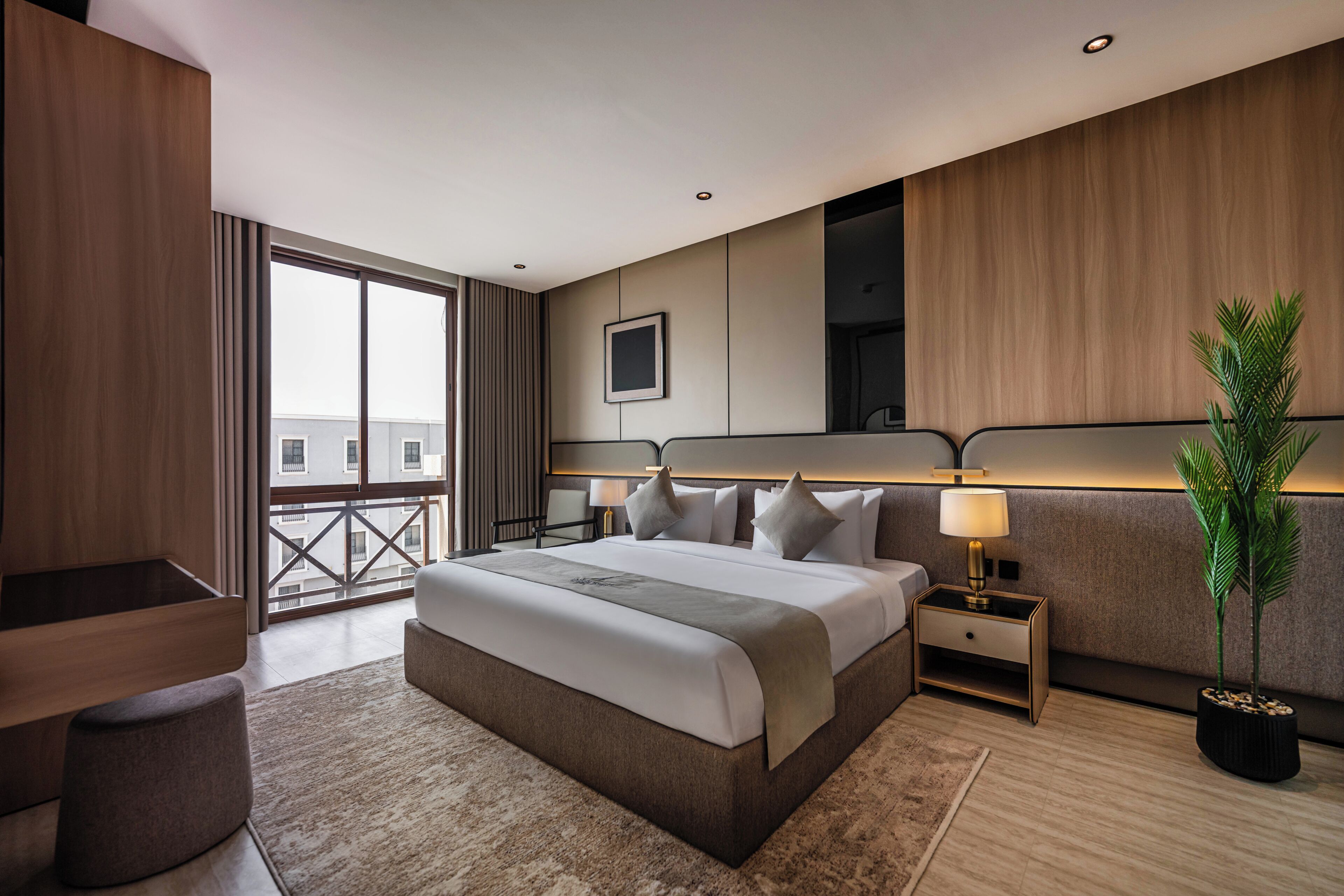A modern hotel room with a large bed, bedside tables, a desk, and a potted plant.