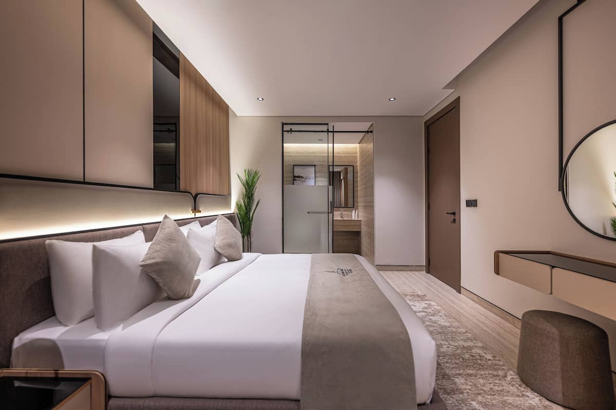 Habitació d'hotel moderna amb un llit gran, una taula de nit, un mirall i un armari.