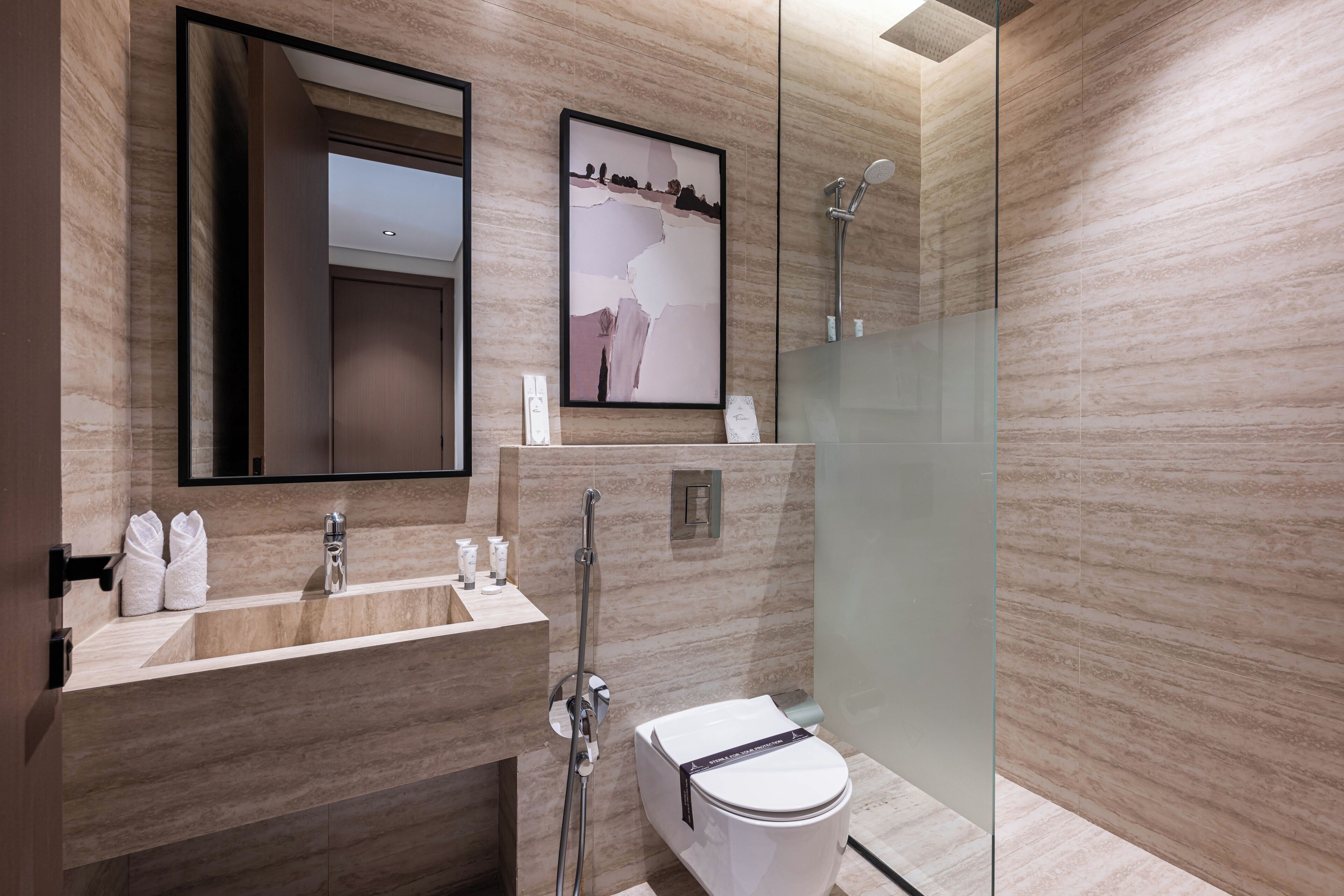 A modern bathroom with a glass-enclosed shower, a sink with toiletries, and a toilet.