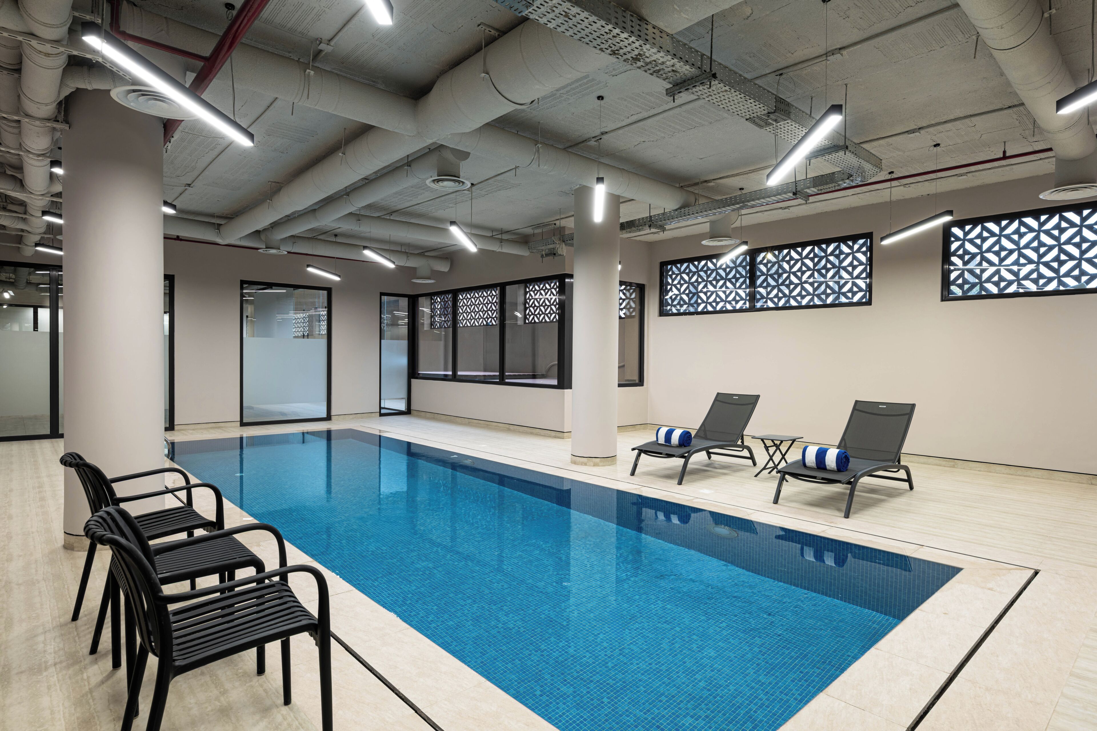 Une piscine intérieure avec des chaises longues noires et un mur orné de motifs.