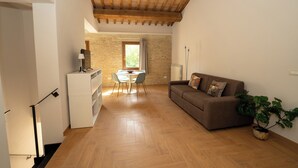 A spacious living area with a herringbone floor, a brown sofa, a dining table with chairs, and a kitchen area in the background. - Beautiful renovated farmhouse in the relaxing Umbrian countryside (Sant'Angelo di Celle)
