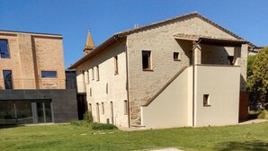 A swimming pool with a clear blue water surface, surrounded by a grassy lawn and a building with a stone facade and a small tower. - Beautiful renovated farmhouse in the relaxing Umbrian countryside (Sant'Angelo di Celle)
