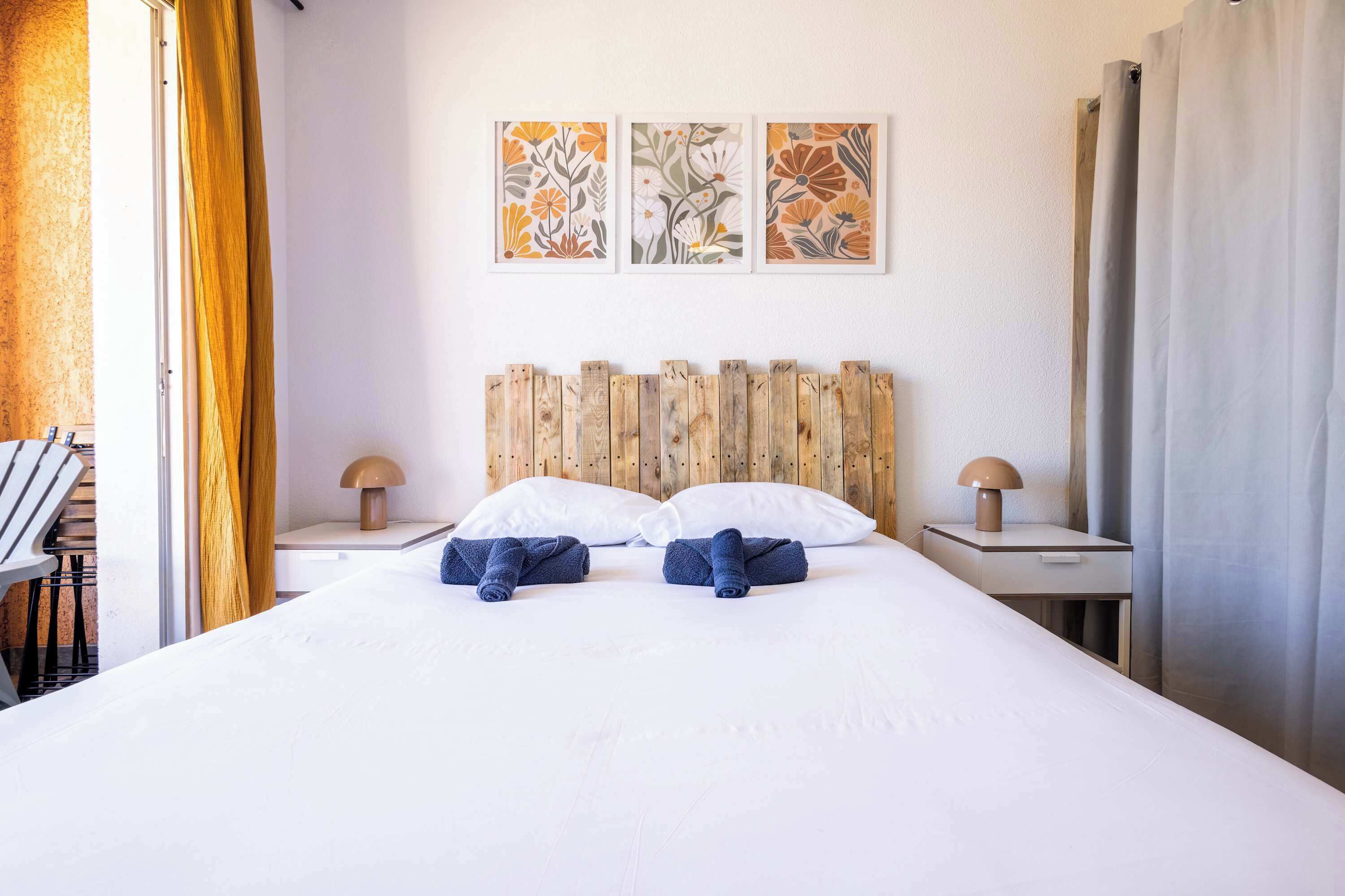 A hotel room with a bed, two nightstands, a wooden headboard, and three wall-mounted floral paintings.