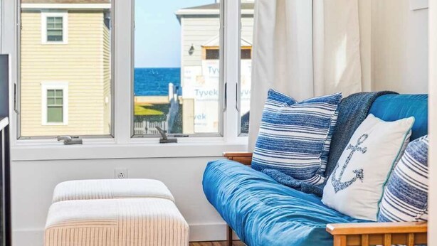 A room with a window, a sofa, and a small ottoman.
