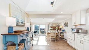 A modern kitchen with white cabinets, a blue accent cabinet, a dining area with a table and chairs, and a view to the outside.