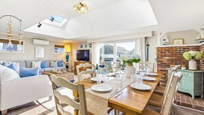A bright room with a dining table set for four, a sofa, a TV, and a skylight.