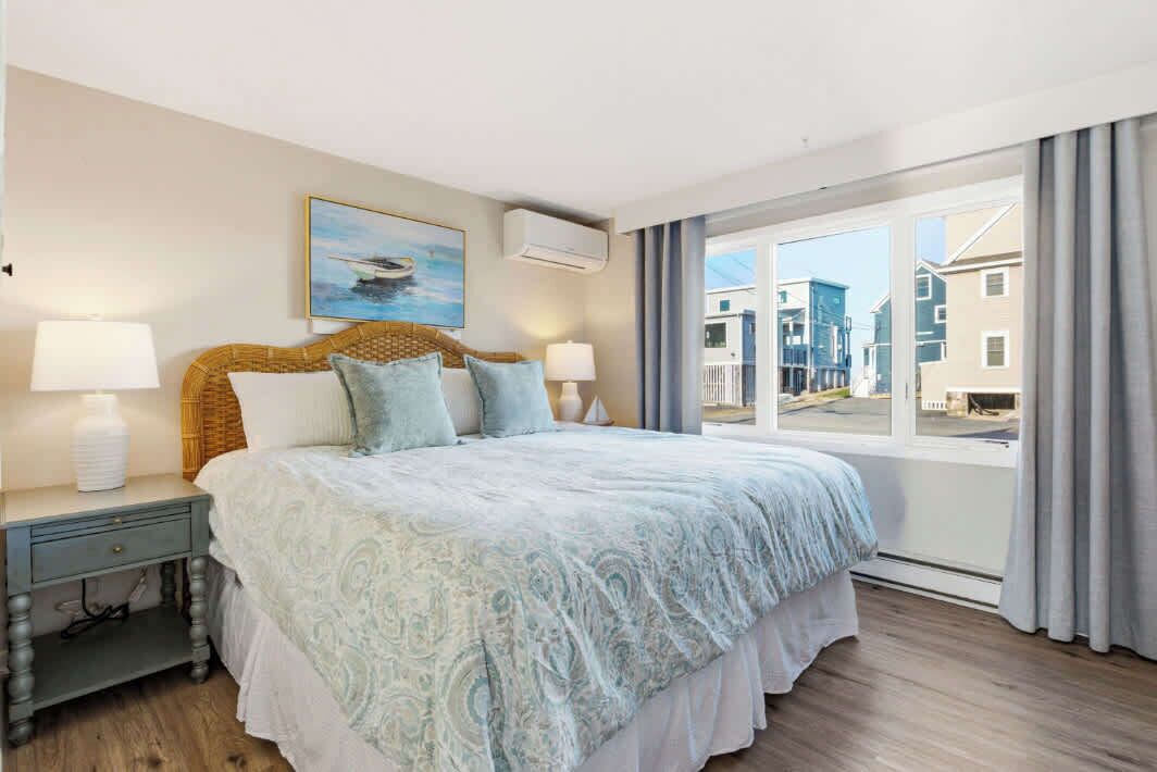 Une chambre à coucher avec un grand lit, deux tables de chevet, une fenêtre avec des rideaux et un tableau au mur.