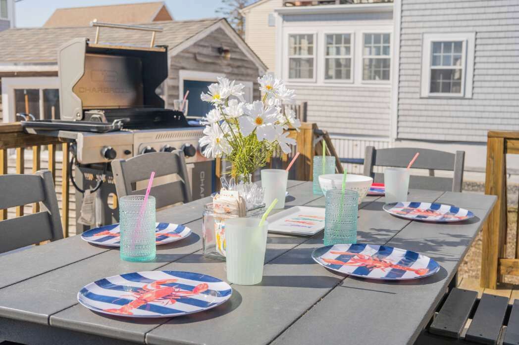 An outdoor dining area with a grill, tables with plates, and drinks.