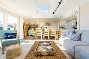 A modern living room with a sofa, ottoman, coffee table, and a dining area with chairs and a table.