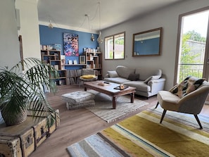 Ein Wohnzimmer mit Sofa, Sessel, Couchtisch, Bücherregal und einem großen Fenster.