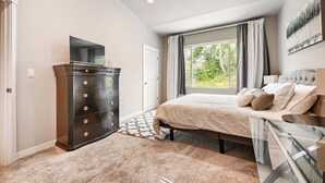 Un dormitorio con cama, cómoda, televisor y ventana con cortinas.