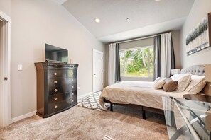 A bedroom with a bed, dresser, TV, and a window with curtains. - New Home near University of Oregon with EV charger (Eugene)