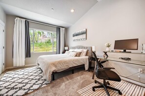 Een slaapkamer met een bed, een bureau, een stoel, een televisie en een raam met gordijnen.