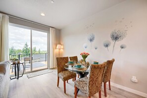 Un comedor con sillas estampadas, una mesa dispuesta para cuatro personas y vistas al balcón exterior a través de una puerta de vidrio.
