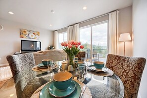 Een eetgedeelte met een glazen tafel, stoelen en een bloemenvaas.