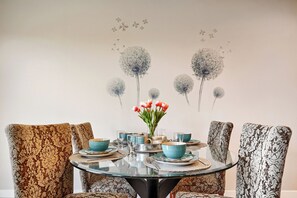 Een eettafel met stoelen, een glazen blad en een vaas met bloemen.