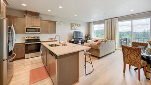 Una cocina moderna con una isla central, un comedor con mesa y sillas, una sala de estar con sofá, y un balcón con vistas.