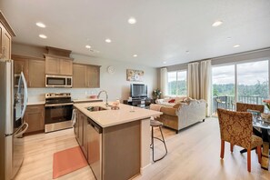 Een moderne keuken met een centraal eiland, een eetgedeelte met tafel en stoelen, een woonkamer met een bank, en een balkon met uitzicht.