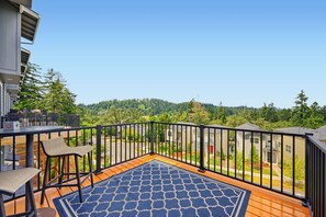 Un balcón con vistas a una zona residencial, una terraza de madera y un tapete azul estampado.
