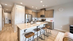 Una cocina moderna con una isla central, taburetes de bar, electrodomésticos de acero inoxidable y un reloj en la pared.