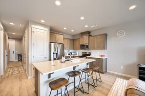 Una cocina moderna con una isla central, taburetes de bar, electrodomésticos de acero inoxidable y un reloj en la pared.
