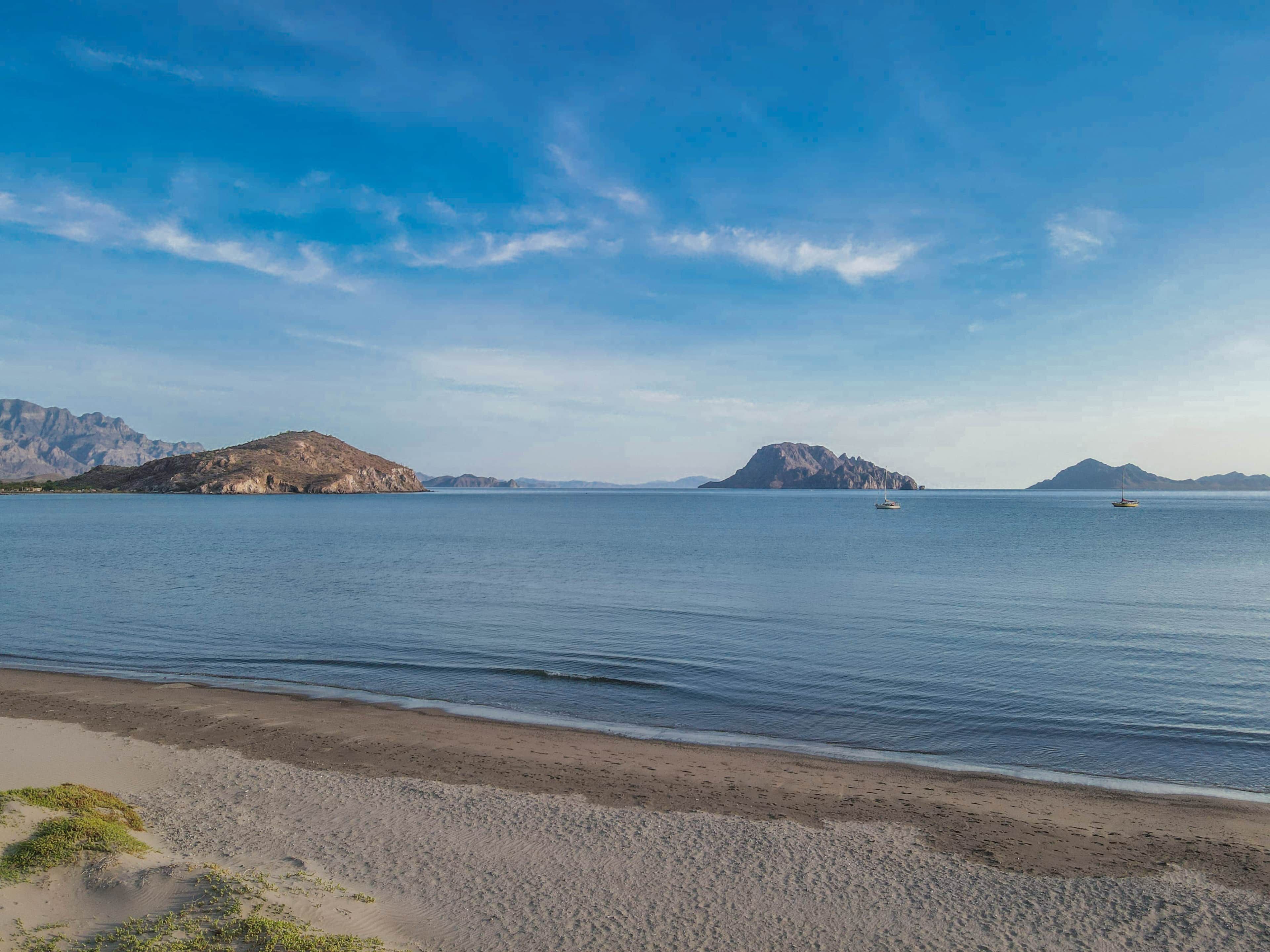 Ein Strand mit ruhigem Wasser, Bergen im Hintergrund und einem kleinen Boot.