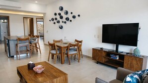 A modern living room with a wooden coffee table, a TV, and a dining area with wooden chairs.