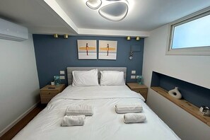 A modern bedroom with a bed, two bedside tables, a window, and artwork on the wall. - לופט אורבני ליד המושבה הגרמנת (Haifa)