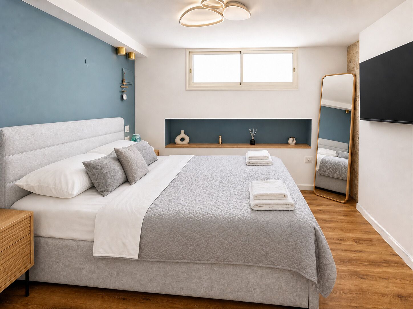 Een moderne slaapkamer met een groot bed, nachtkastjes, een raam, een spiegel en een plafondlamp.
